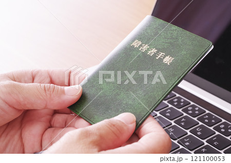 パソコンの前で障害者手帳を持つ女性 パソコンの前で障害者手帳を持つ女性 121100053
