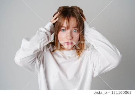A young woman with light brown hair and blue eyes expresses surprise in a minimalist studio A young woman with light brown hair and blue eyes expresses surprise in a minimalist studio 121100062