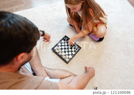 A young girl is playing chess with her father on the floor A young girl is playing chess with her father on the floor 121100096