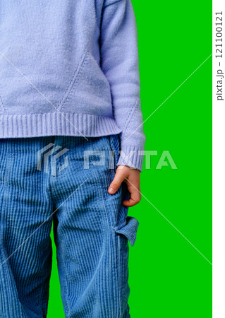 A child in a light purple sweater with blue pants stands against a vibrant green background A child in a light purple sweater with blue pants stands against a vibrant green background 121100121
