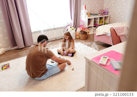 A father and daughter play a game together on the floor of a bedroom A father and daughter play a game together on the floor of a bedroom 121100133