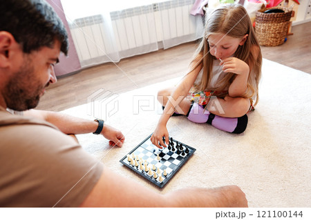 A young girl is playing chess with a man on a white rug A young girl is playing chess with a man on a white rug 121100144