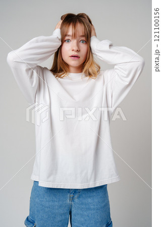 A young woman with light brown hair and blue eyes expresses surprise in a minimalist studio A young woman with light brown hair and blue eyes expresses surprise in a minimalist studio 121100156