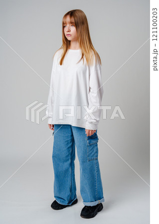 A young person wearing a white long-sleeve shirt and blue cargo pants stands confidently against a neutral background A young person wearing a white long-sleeve shirt and blue cargo pants stands confidently against a neutral background 121100203