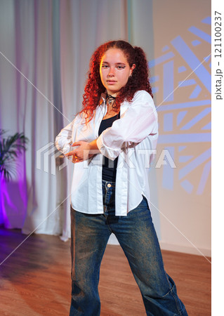 A young woman with red hair stands on a stage, looking confident with her arms crossed A young woman with red hair stands on a stage, looking confident with her arms crossed 121100237