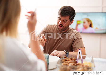 A man is eating at a table, while a woman watches A man is eating at a table, while a woman watches 121100446