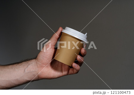 A hand holding a disposable coffee cup against a dark background A hand holding a disposable coffee cup against a dark background 121100473