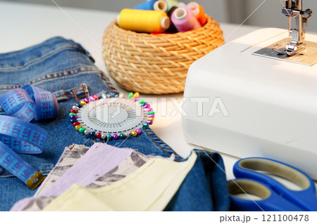 Sewing machine in use on a wooden table, stitching a light fabric in a well-lit indoor workspace 121100478