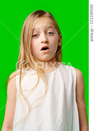 Young girl in a white dress surprised against a bright green background 121100500