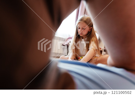 A young girl sits on the floor, looking down thoughtfully, from a low-angle perspective 121100502