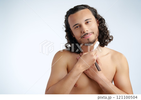 A man with curly hair grooming his beard in a well-lit space while using a straight razor A man with curly hair grooming his beard in a well-lit space while using a straight razor 121100504