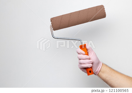 Hand with a paint roller preparing to paint a wall in a bright and clean room during a home improvement project Hand with a paint roller preparing to paint a wall in a bright and clean room during a home improvement project 121100565