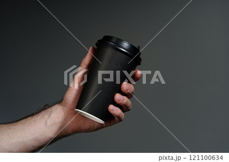 A hand holding a disposable coffee cup against a dark background 121100634