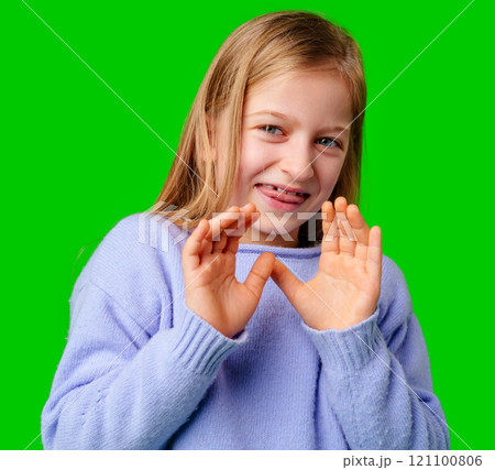A young girl in a light purple sweater poses with her hand extended, signaling a stop gesture against green background A young girl in a light purple sweater poses with her hand extended, signaling a stop gesture against green background 121100806