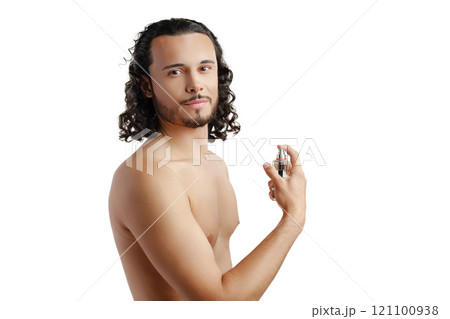 A young man with curly hair applying fragrance after a shower while smiling at the camera 121100938