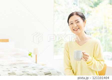 ベッドでコーヒーを飲むミドル女性 121101404