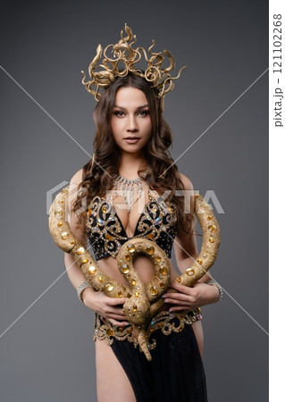 Model poses elegantly with a snake in ornate gold and black attire 121102268