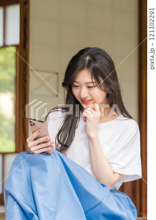古民家の縁側でスマホをタッチする若い女性　ネットショッピングを楽しむ若い女性 121102291