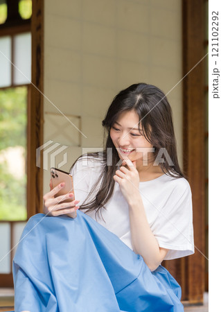 古民家の縁側でスマホをタッチする若い女性 ネットショッピングを楽しむ若い女性 古民家の縁側でスマホをタッチする若い女性 ネットショッピングを楽しむ若い女性 121102292