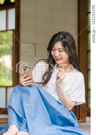 古民家の縁側でスマホをタッチする若い女性　ネットショッピングを楽しむ若い女性 121102295