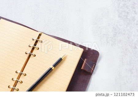 リング式のシステム手帳を開いてデスクワークをしているイメージ 121102473