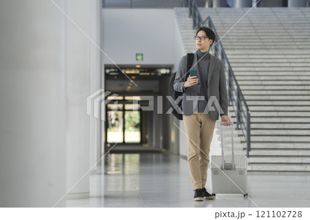 キャリーバッグを引いて歩くスマートフォンを持った40代の男性 121102728