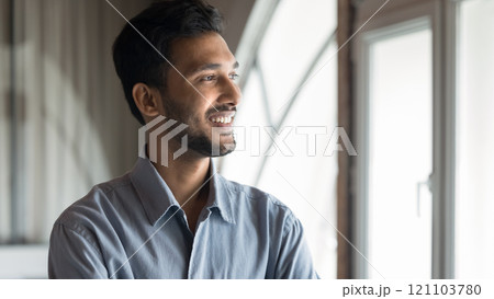 Indian man looking out of window with thoughtful expression Indian man looking out of window with thoughtful expression 121103780