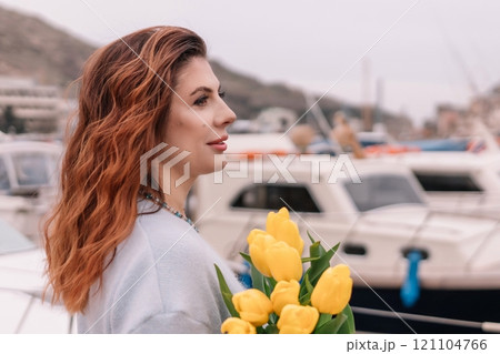 Woman holds yellow tulips in harbor with boats docked in the background., overcast day, yellow sweater, mountains Woman holds yellow tulips in harbor with boats docked in the background., overcast day, yellow sweater, mountains 121104766
