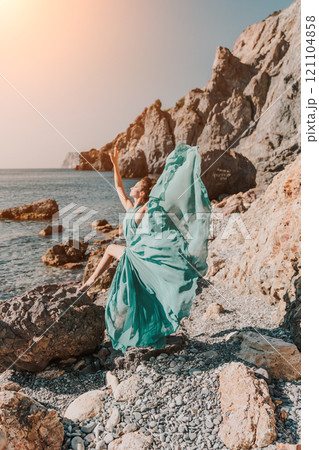 Woman green dress sea. Woman in a long mint dress posing on a beach with rocks on sunny day. Girl on the nature on blue sky background. Woman green dress sea. Woman in a long mint dress posing on a beach with rocks on sunny day. Girl on the nature on blue sky background. 121104858