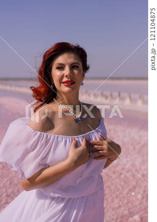 Woman Pink Salt Lake Summer Fashion - A woman in a white dress poses in a pink salt lake during summer. She is smiling and looking at the camera. The lake is a beautiful pink color. 121104875
