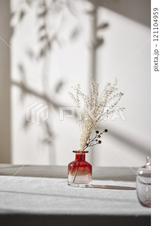Warm sunlight streaming in through the window, beige background, flowers, vases, and a table with plants. Harmony of light and shadow. Warm sunlight streaming in through the window, beige background, flowers, vases, and a table with plants. Harmony of light and shadow. 121104959