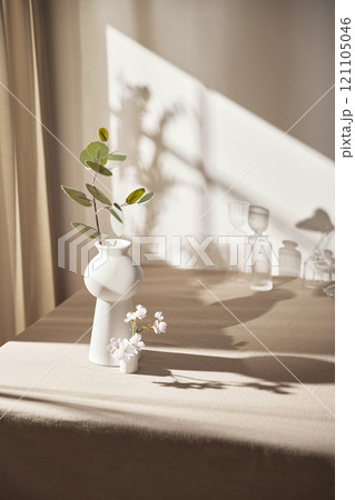 Warm sunlight streaming in through the window, beige background, flowers, vases, and a table with plants. Harmony of light and shadow. Warm sunlight streaming in through the window, beige background, flowers, vases, and a table with plants. Harmony of light and shadow. 121105046