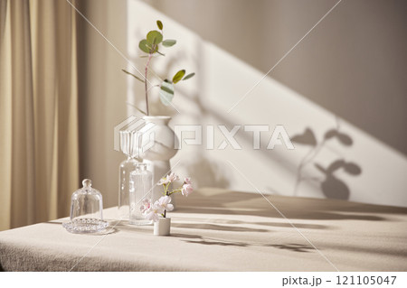 Warm sunlight streaming in through the window, beige background, flowers, vases, and a table with plants. Harmony of light and shadow. 121105047