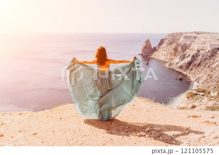 Woman green dress sea. Female dancer posing on a rocky outcrop high above the sea. Girl on the nature on blue sky background. Fashion photo. Woman green dress sea. Female dancer posing on a rocky outcrop high above the sea. Girl on the nature on blue sky background. Fashion photo. 121105575