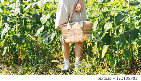 Woman standing at outdoors flower park fields hand holding fashion woven bag Woman standing at outdoors flower park fields hand holding fashion woven bag 121105783