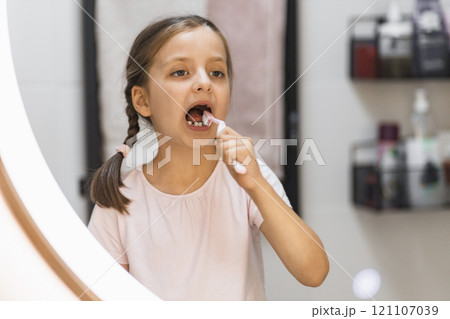 Caucasian girl with missing milk teeth brushing teeth in bathroom. She looks attentively in mirror, focusing on oral hygiene. Concept of childhood routines and dental care. Caucasian girl with missing milk teeth brushing teeth in bathroom. She looks attentively in mirror, focusing on oral hygiene. Concept of childhood routines and dental care. 121107039