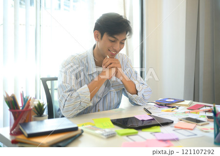 Smiling male UX designer working on app design ideas with detailed sketches spread across the desk Smiling male UX designer working on app design ideas with detailed sketches spread across the desk 121107292