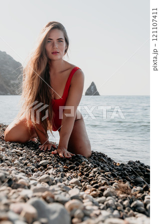 Woman in Red Bathing Suit Kneeling on a Pebble Beach 121107411