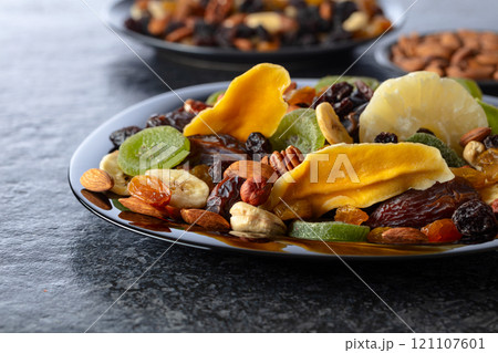 Dried tropical fruits, nuts, and raisins in black plate. Dried tropical fruits, nuts, and raisins in black plate. 121107601