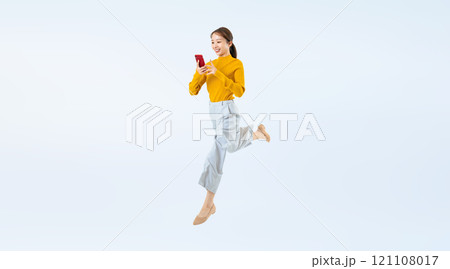 スマホを見ながらジャンプする女性の全身写真 スマホを見ながらジャンプする女性の全身写真 121108017