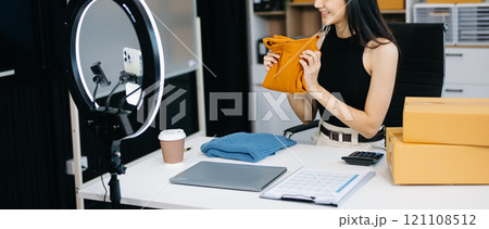 Fashion blogger concept, Young Asian women selling clothes on video streaming.Startup small business SME, using smartphone or tablet taking receive and checking 121108512