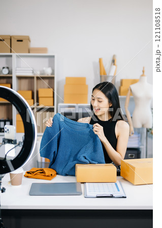 Fashion blogger concept, Young Asian women selling clothes on video streaming.Startup small business SME, using smartphone or tablet taking receive and checking Fashion blogger concept, Young Asian women selling clothes on video streaming.Startup small business SME, using smartphone or tablet taking receive and checking 121108518