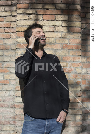 Man laughing while talking on the phone against a brick wall. Man laughing while talking on the phone against a brick wall. 121108696