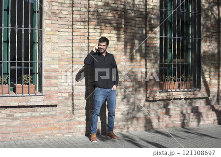 Man laughing while talking on the phone against a brick wall. Man laughing while talking on the phone against a brick wall. 121108697