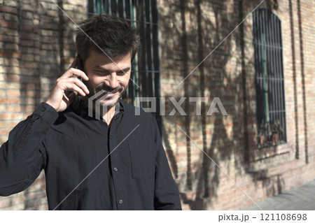 Man laughing while talking on the phone against a brick wall. Man laughing while talking on the phone against a brick wall. 121108698