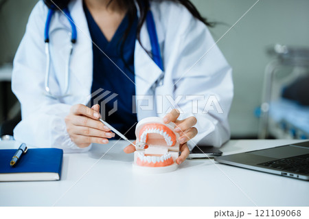 Dentist sitting at table with jaw samples tooth model and working with tablet and laptop in dental modern office 121109068