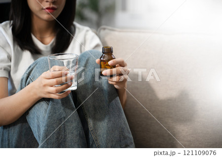 Young Asian Woman sitting in the sofa with a large number of pills Depressed woman wants to kill herself by drug overdose 121109076