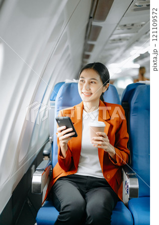 Asian businesswoman or entrepreneur in a formal suit on an airplane sitting in business class using a phone, computer laptop. Travel in style, work 121109572