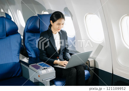 Attractive Asian female passenger of airplane sitting in comfortable seat while working laptop and tablet with mock up area using wireless connection. 121109952