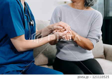 Young nurse helping elderly woman walk in the room, holding his hand, supporting. Treatment and rehabilitation after injury in assisted living facility Young nurse helping elderly woman walk in the room, holding his hand, supporting. Treatment and rehabilitation after injury in assisted living facility 121110525